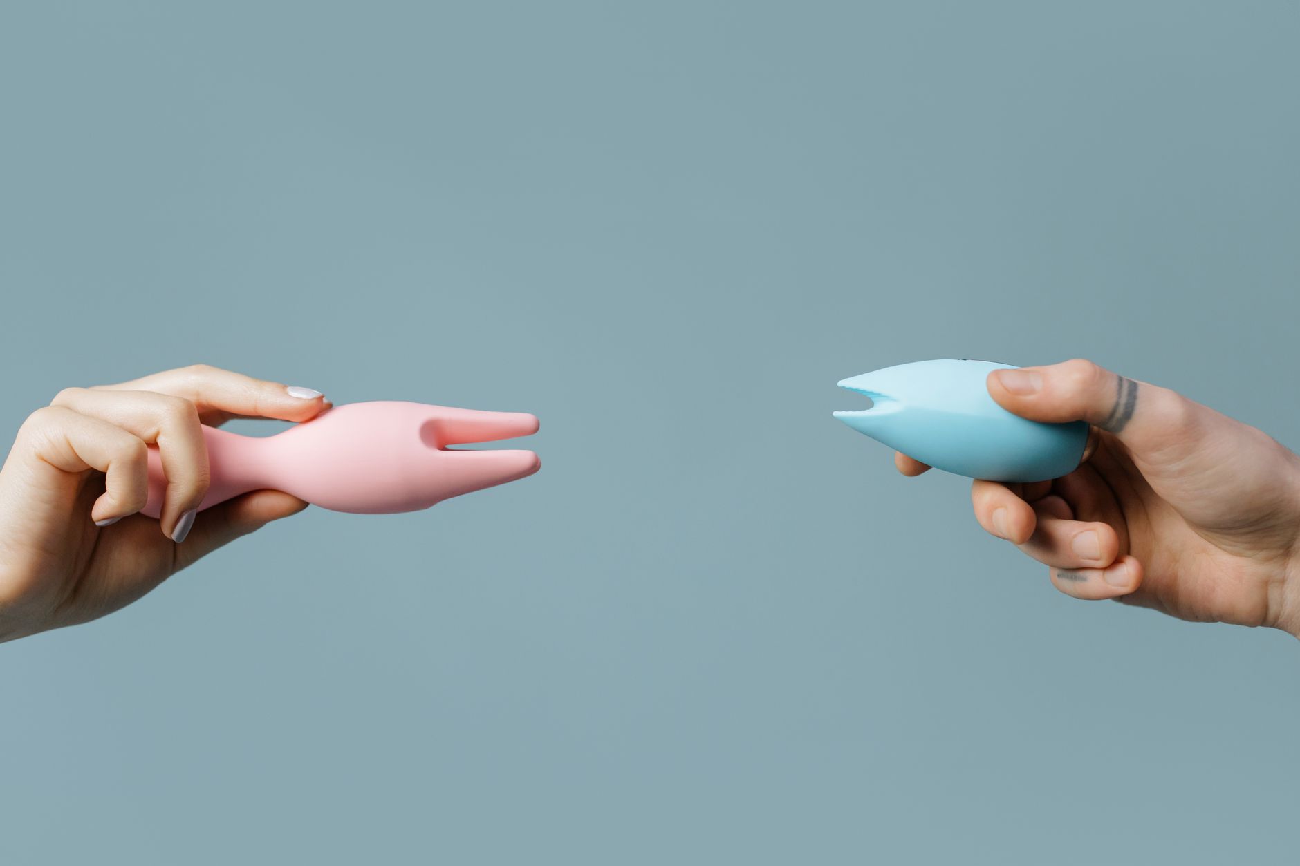 Two hands holding colorful vibrators against a soft pastel background, symbolizing choice and comfort.
