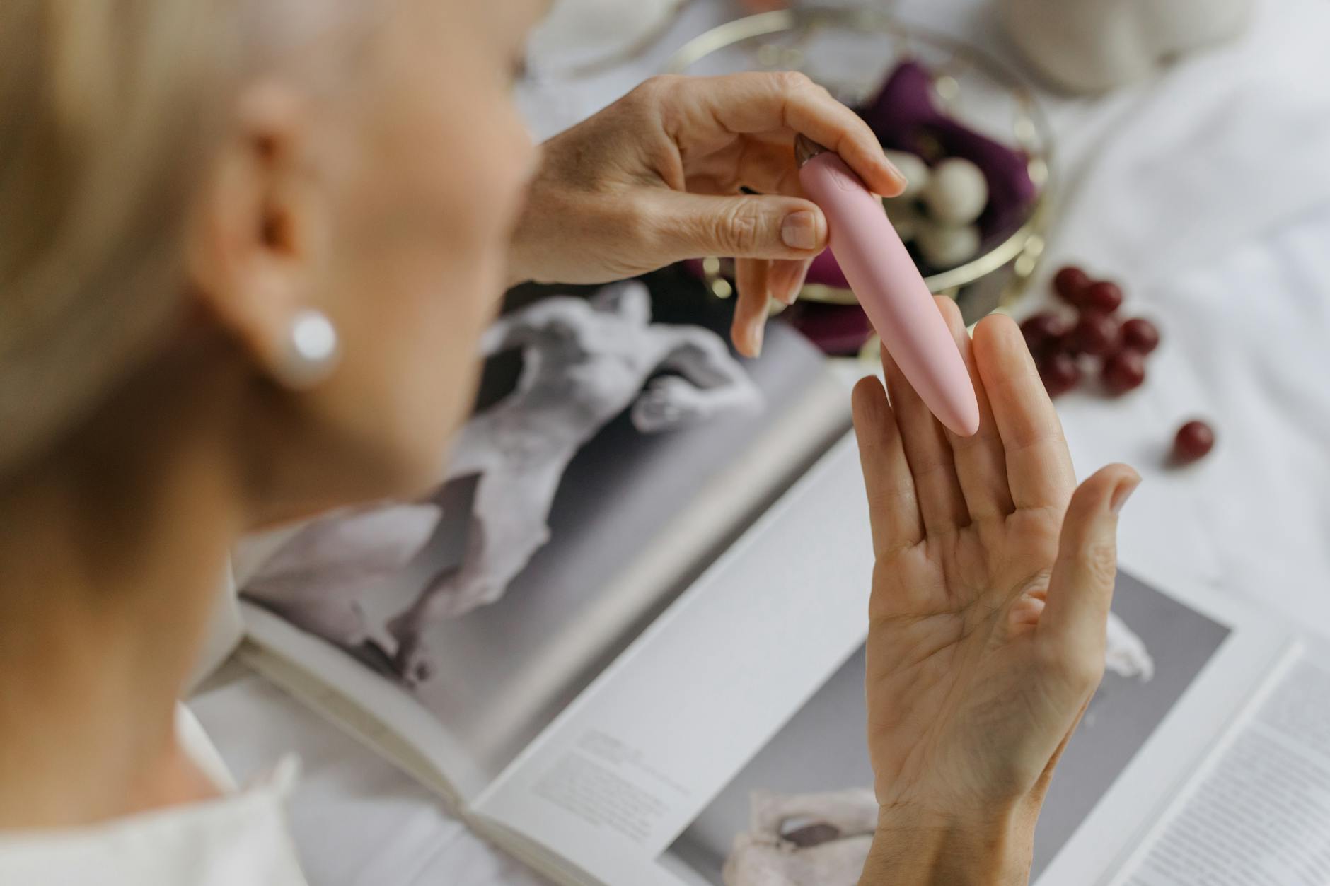 Close-up of a woman holding a pink vibrator with art books nearby, capturing the intimate moment of rediscovering sensation.
