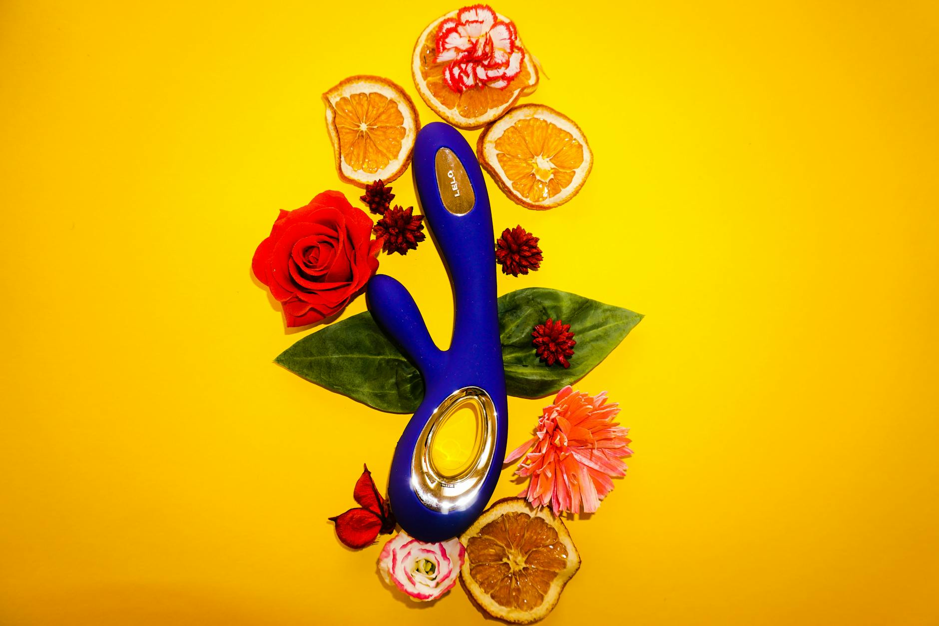 A blue lemon vibrator surrounded by flowers and citrus slices on a bright yellow surface